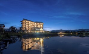 A multi-story hotel with a modern architectural design, situated by a calm lake with reflections.