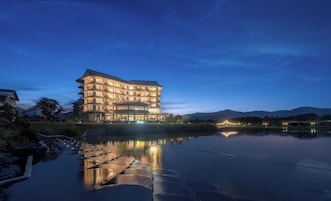 Un hotel de varios pisos con un diseño arquitectónico moderno, ubicado junto a un lago tranquilo con reflejos.