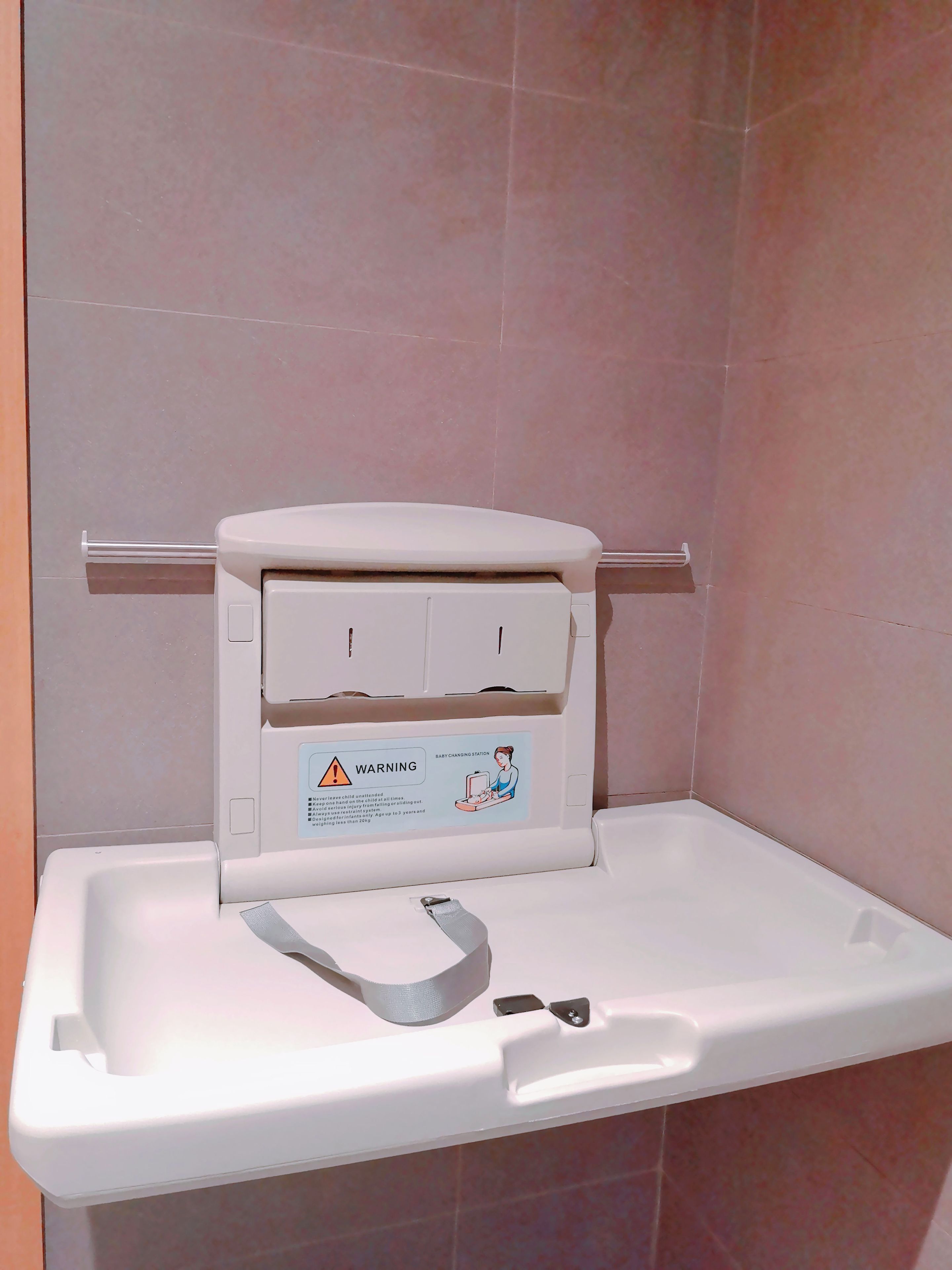 A baby changing station with a warning label and a safety strap.