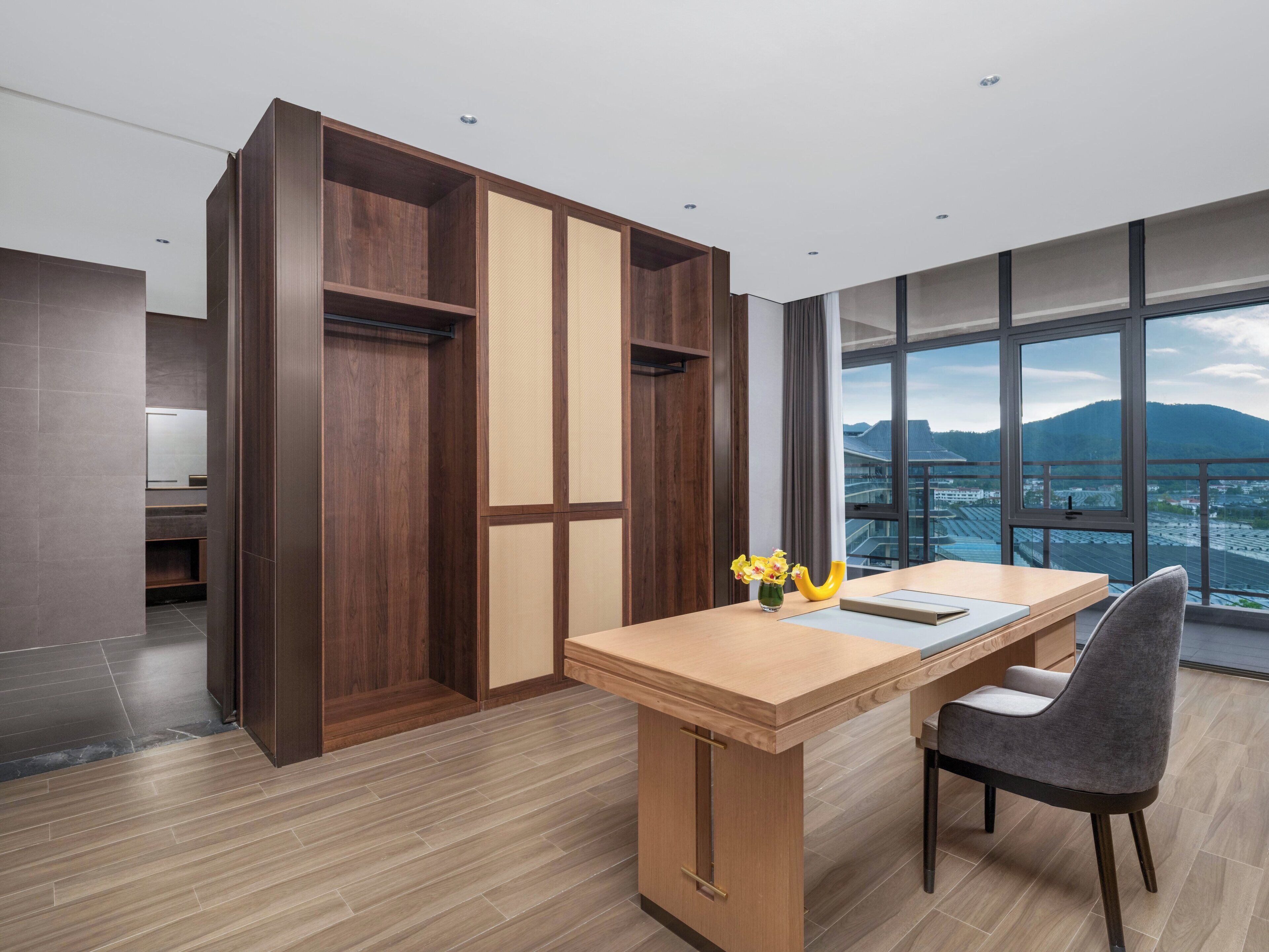 A modern office space with a wooden desk, a chair, and a view of a cityscape through large windows.