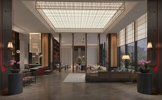 Un vestíbulo de hotel moderno con techo alto, ventanas grandes y una zona de estar central.