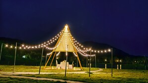 Ein Zelt mit Lichterketten, einem Tisch und Stühlen in einem offenen Feld bei Nacht.