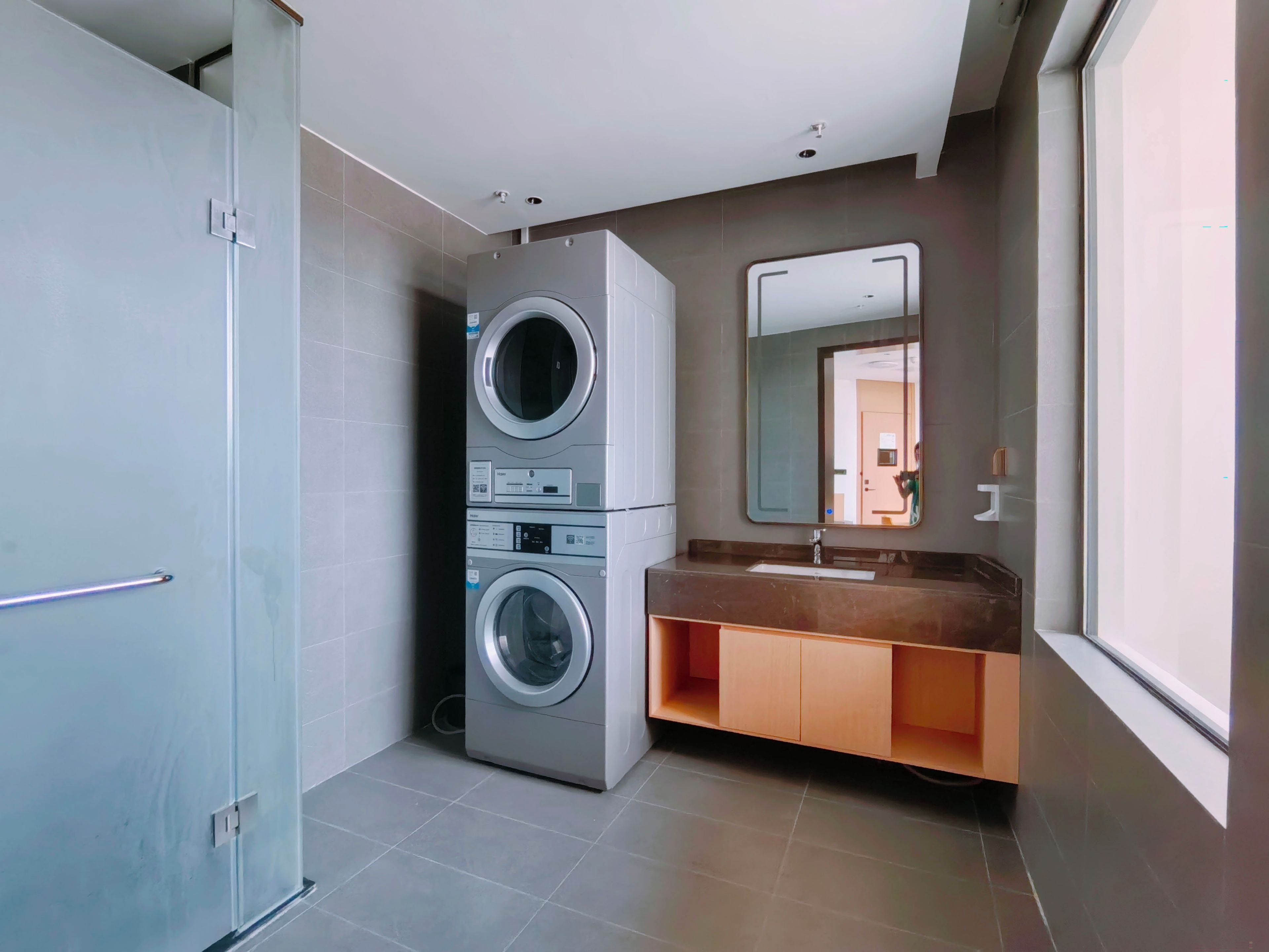 A modern bathroom with a grey washing machine, a sink, and a mirror.