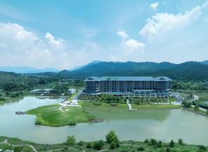 A Holiday Inn hotel with a modern design, surrounded by a lake and mountains. - Holiday Inn Ganzhou Orchid Town by IHG (Ganzhou)