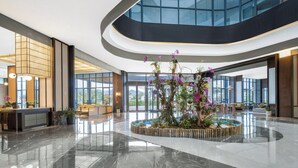 Eine moderne Lobby mit einem zentralen Garten, einer gewölbten Decke und großen Fenstern.