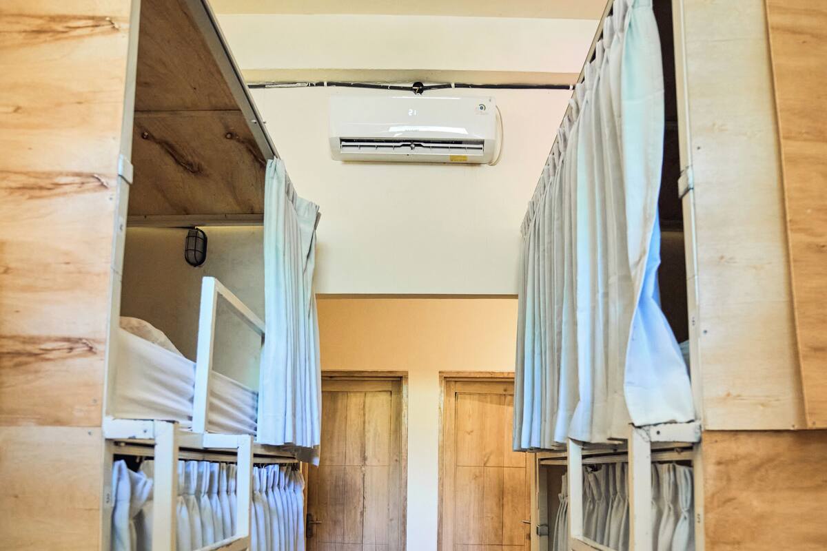A narrow corridor with bunk beds on either side, wooden walls, and a ceiling-mounted air conditioner.