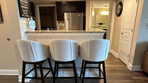 Una cocina moderna con una isla central, tres taburetes de bar y un refrigerador.