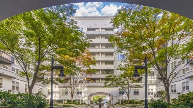 Un edificio de varios pisos con un patio central, rodeado de árboles y una fuente.