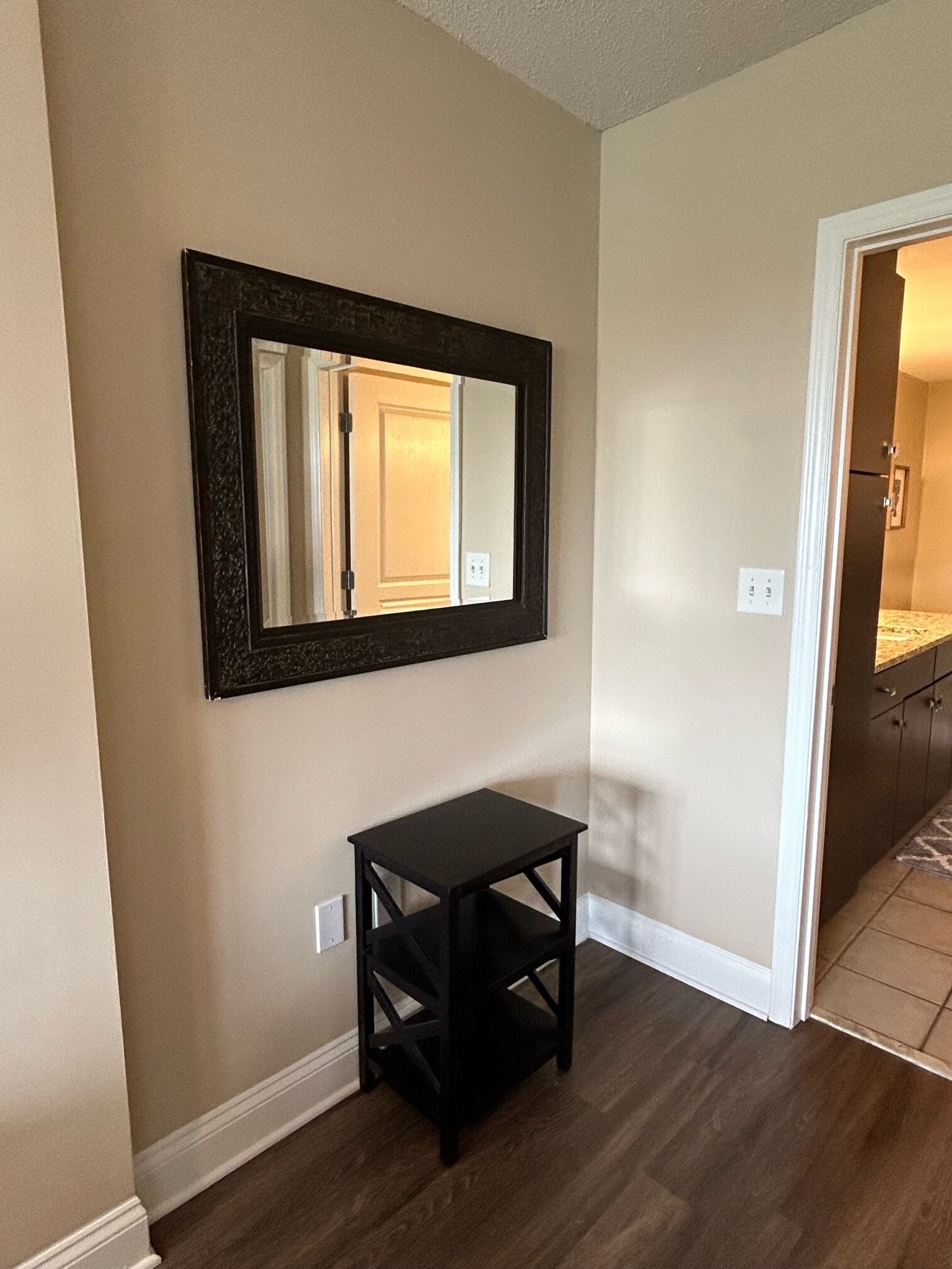 A hallway with a dark-framed mirror, a small black table, and a door leading to another room.