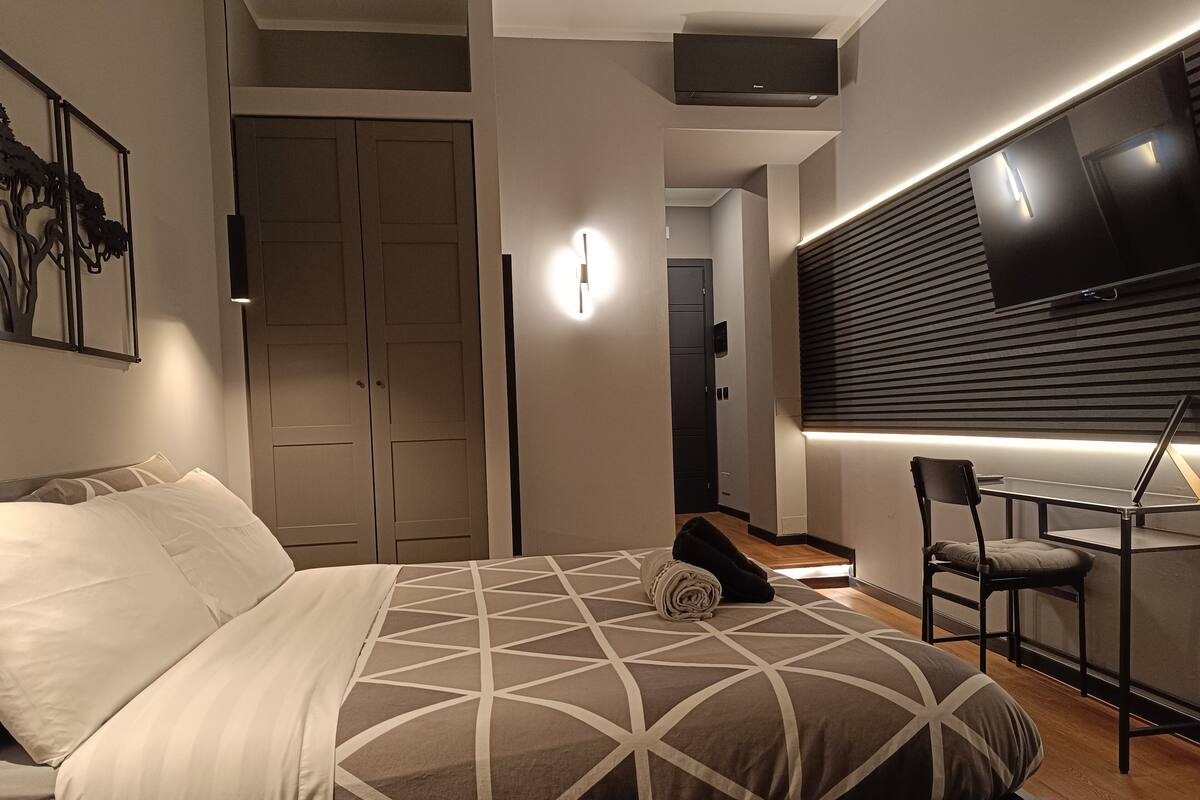 A modern bedroom with a bed, a desk, and a TV.