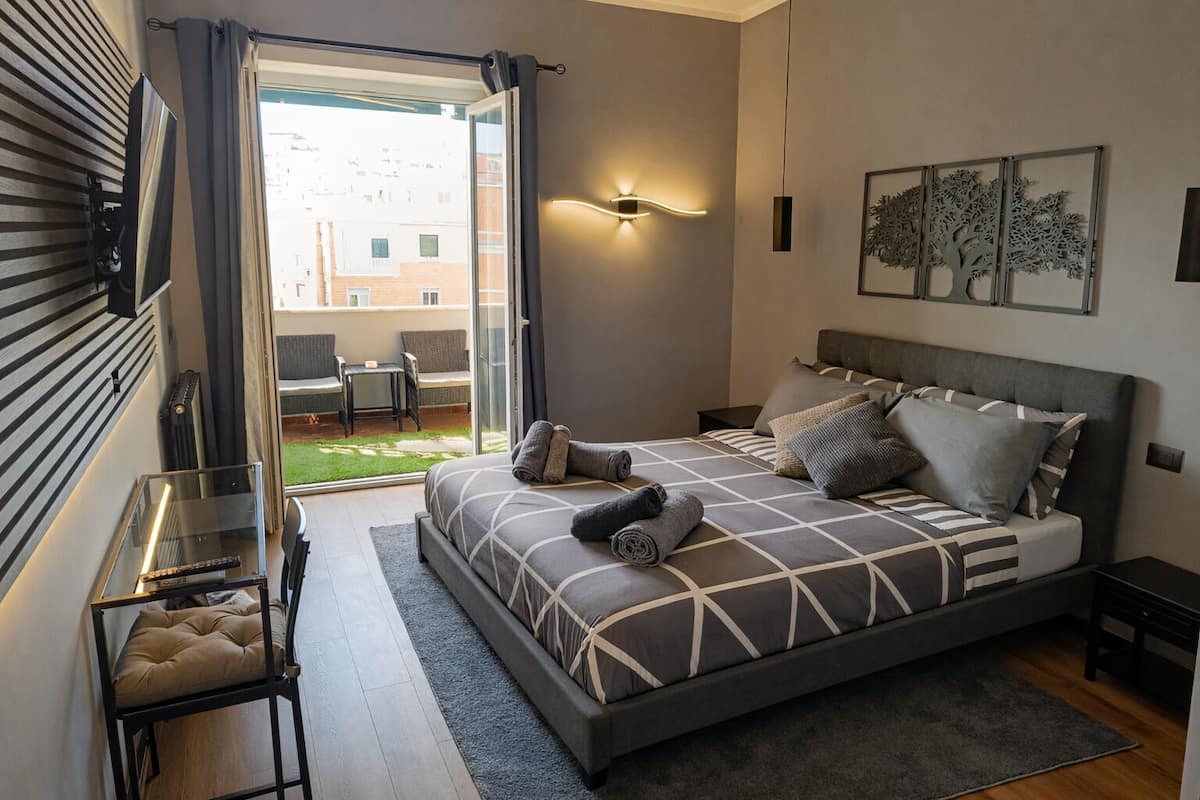 A modern bedroom with a large bed, a view of the outdoors, and a balcony.