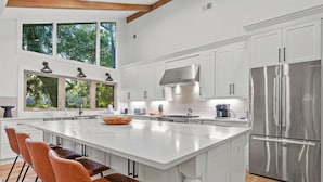 A modern kitchen with a large island, white cabinetry, stainless steel appliances, and a view of greenery through large windows. - Upscale Coastal Ranch ~ Private Pool & Spa ~ 13 Planters Wood Ct ~ Sleeps 10 (Hilton Head Island)
