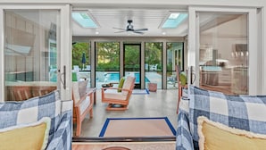 A modern living room with a view of a swimming pool, a ceiling fan, and a glass door leading to the outdoors. - Upscale Coastal Ranch ~ Private Pool & Spa ~ 13 Planters Wood Ct ~ Sleeps 10 (Hilton Head Island)