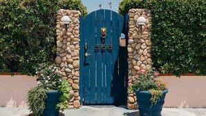A blue gate with a stone wall, number 556, and two potted plants.