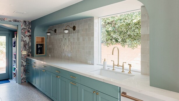 A kitchen with teal cabinets, a white countertop, and a window with a view of greenery.