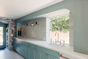 A kitchen with teal cabinets, a white countertop, and a window with a view of greenery.