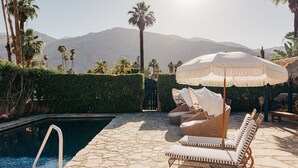 A pool area with stone flooring, lounge chairs, and a canopy.