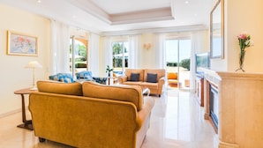 A spacious living room with a large sofa, a television, and a fireplace. - Villa Monte Rei Golf (Vila Real Santo Antonio)