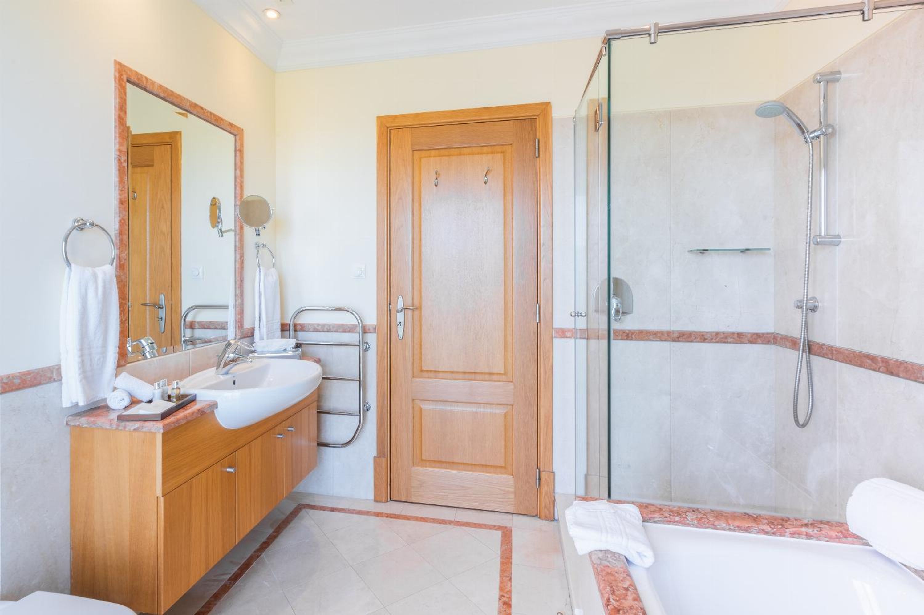 A bathroom with a wooden vanity, a large mirror, a bathtub, and a glass-enclosed shower area.