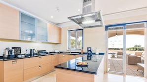 A modern kitchen with a central island, wooden cabinets, and a large window. - Villa Monte Rei Golf (Vila Real Santo Antonio)