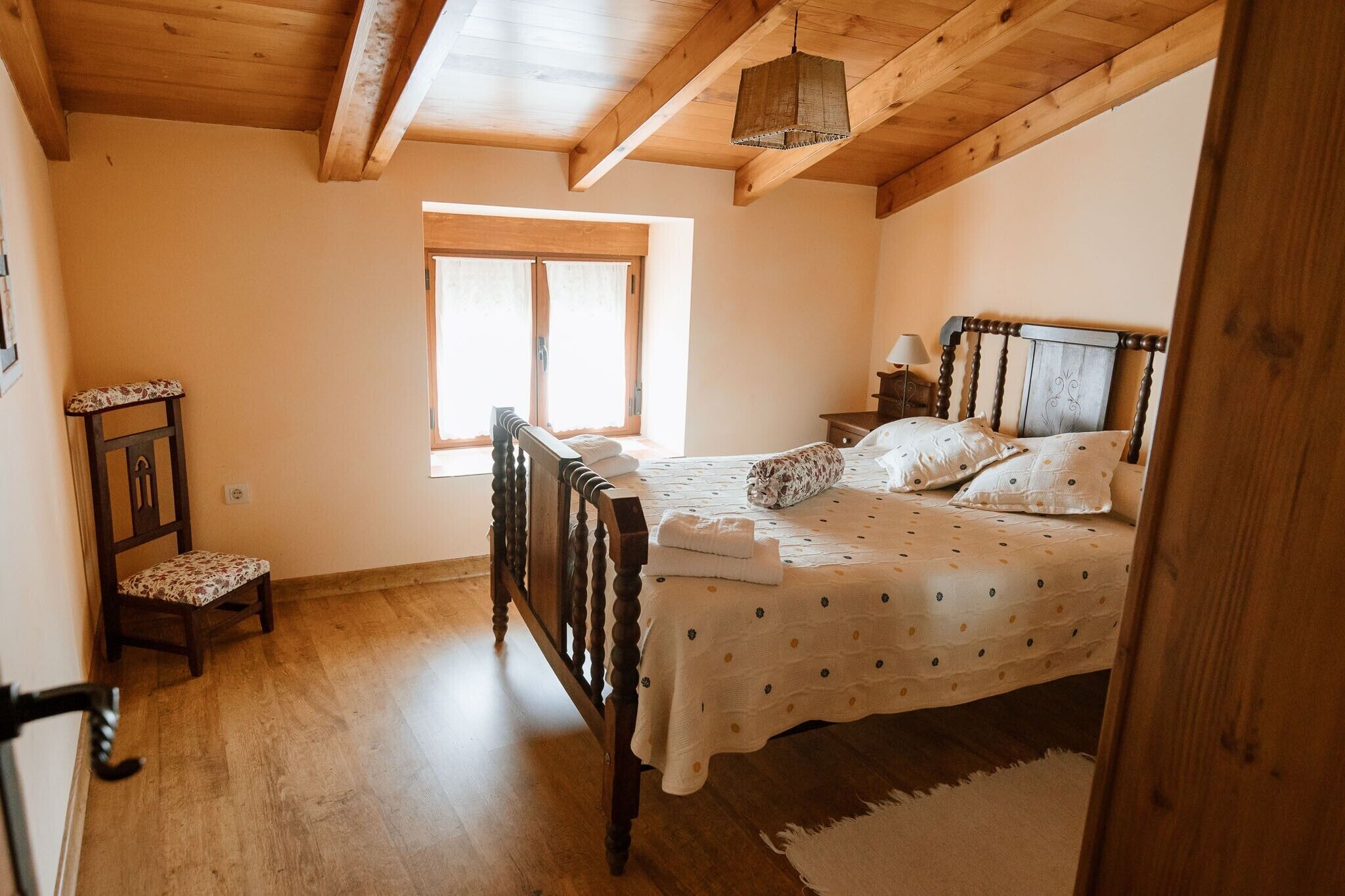 A bedroom with a wooden bed, a window, a chair, and a nightstand.