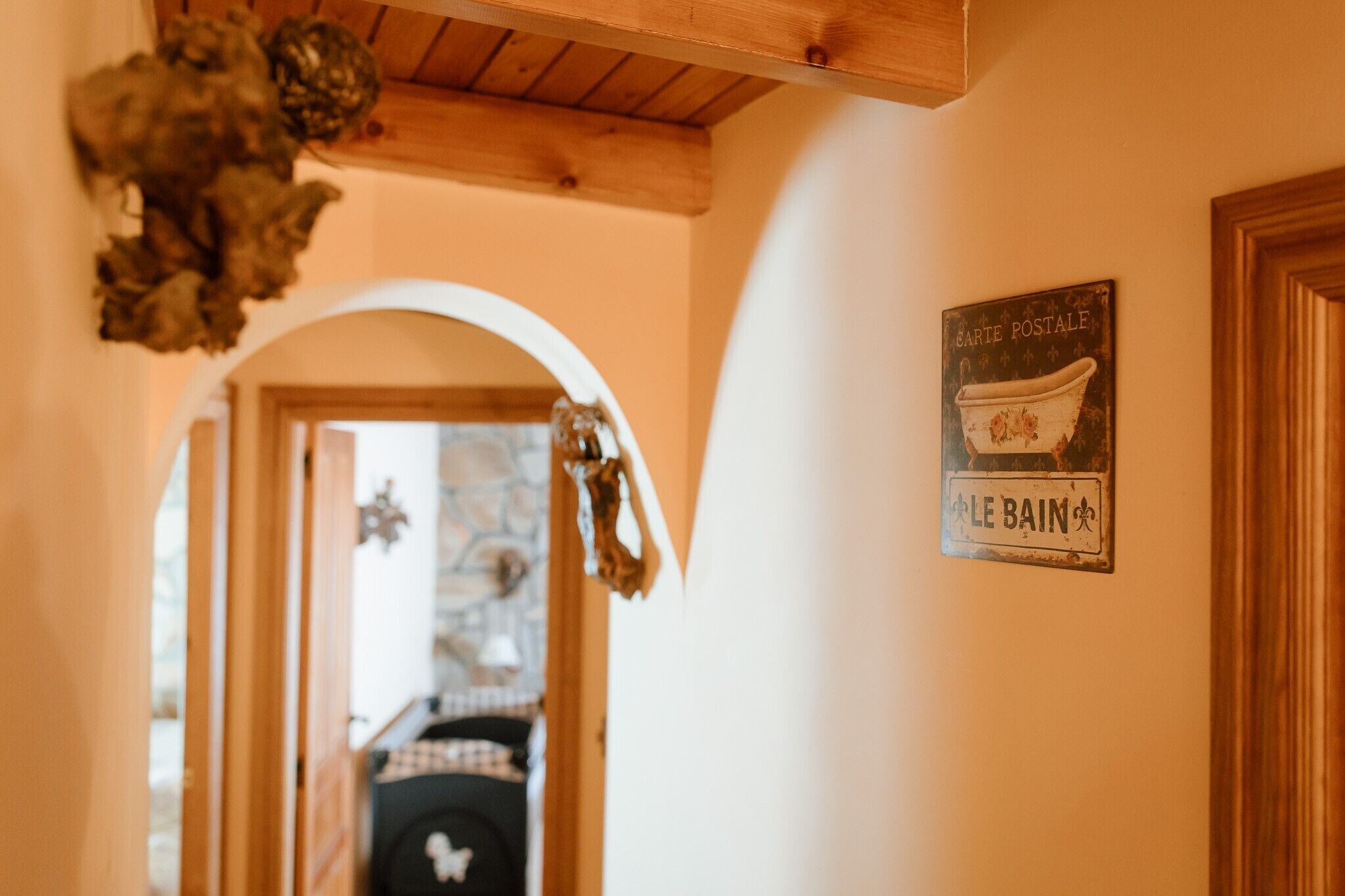 Un pasillo con techo de madera, un letrero que dice 'Carte Postale Le Bain' y un vano que da a otra habitación.