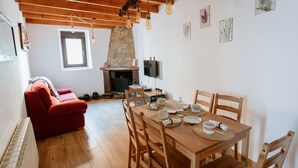 Un salon chaleureux avec une cheminée, une table à manger dressée pour quatre personnes et un canapé rouge.