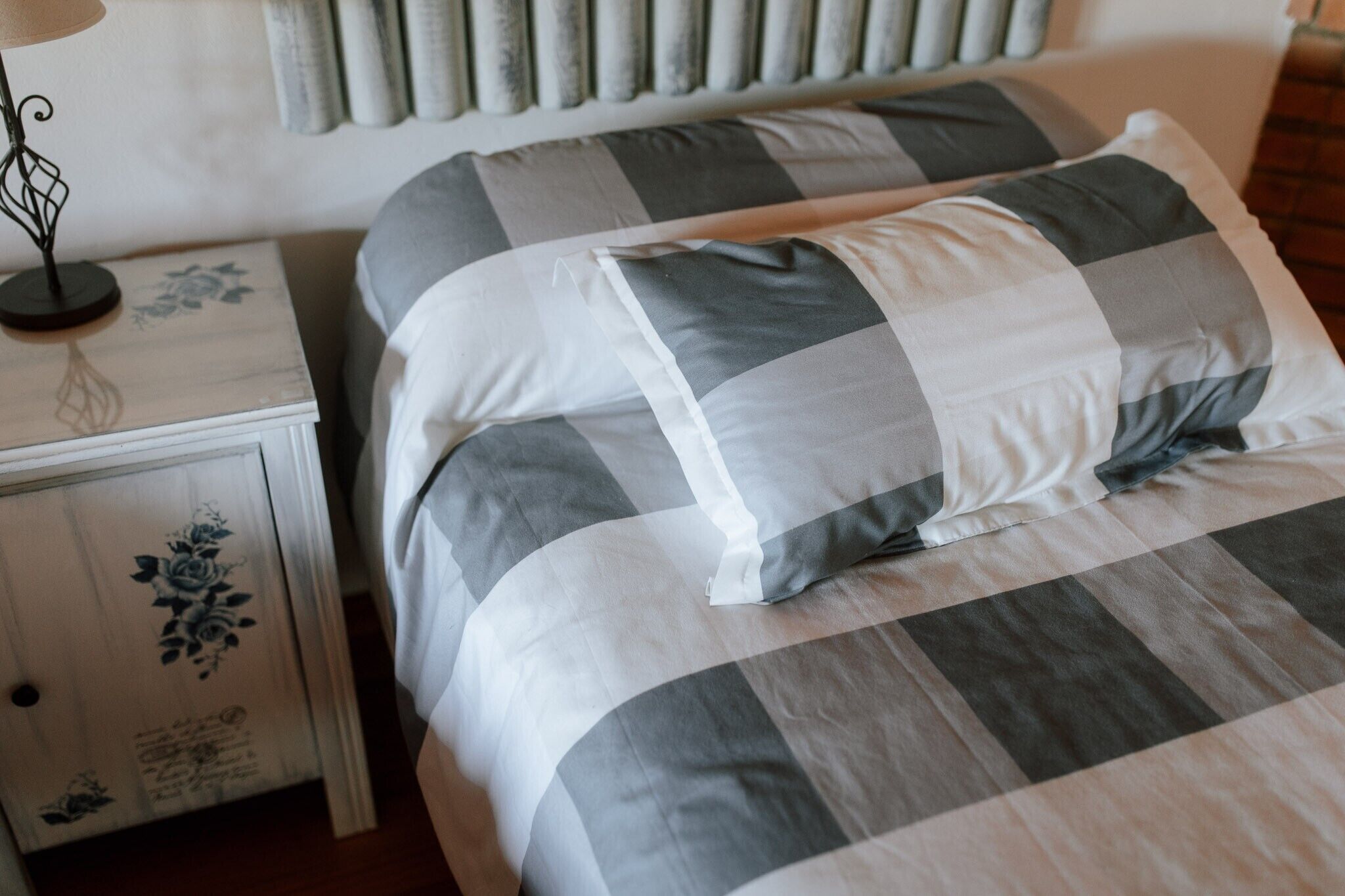 Una cama con colcha a cuadros, una mesita de noche con lámpara y una mesita con diseño floral.