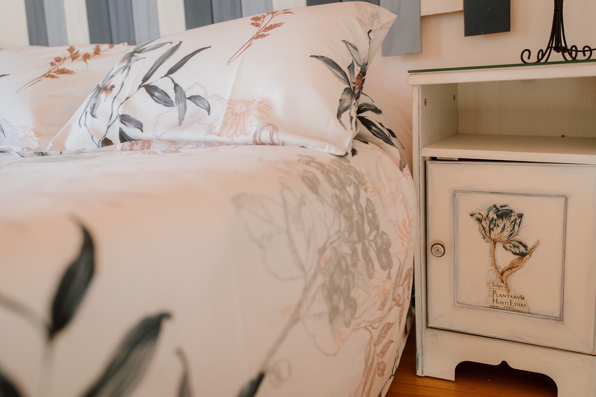 Een bed met bloemenbeddengoed, een nachtkastje met een ingelijste foto en een wandlamp.