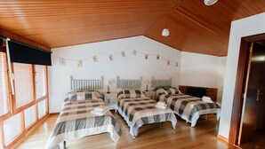 Une chambre avec trois lits, un plancher en bois, un plafond en pente et une guirlande de cartes accrochée au mur.