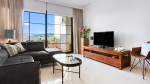 A modern living room with a sofa, a glass coffee table, a TV on a wooden cabinet, and a view through large windows. - 'Gadea 11-2' Apartment with Sea Views, Wi-Fi, and Air Conditioning (Altea)