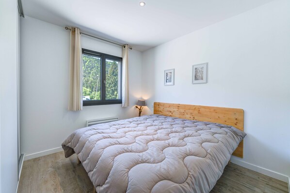 A bedroom with a bed, a window with curtains, a bedside lamp, and two framed pictures on the wall. - 'Aux Pieds Des Pistes - Appt A' Apartment with Mountain View, Wi-Fi, and Air Conditioning (Ax-les-Thermes)