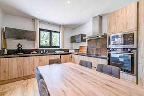A modern kitchen with wooden cabinets, a large island with seating, a built-in oven, and a window providing natural light. - 'Aux Pieds Des Pistes - Appt A' Apartment with Mountain View, Wi-Fi, and Air Conditioning (Ax-les-Thermes)
