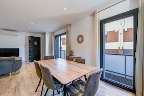 Zona pranzo moderna con tavolo e sedie in legno, televisione e ampia finestra con vista sugli edifici.