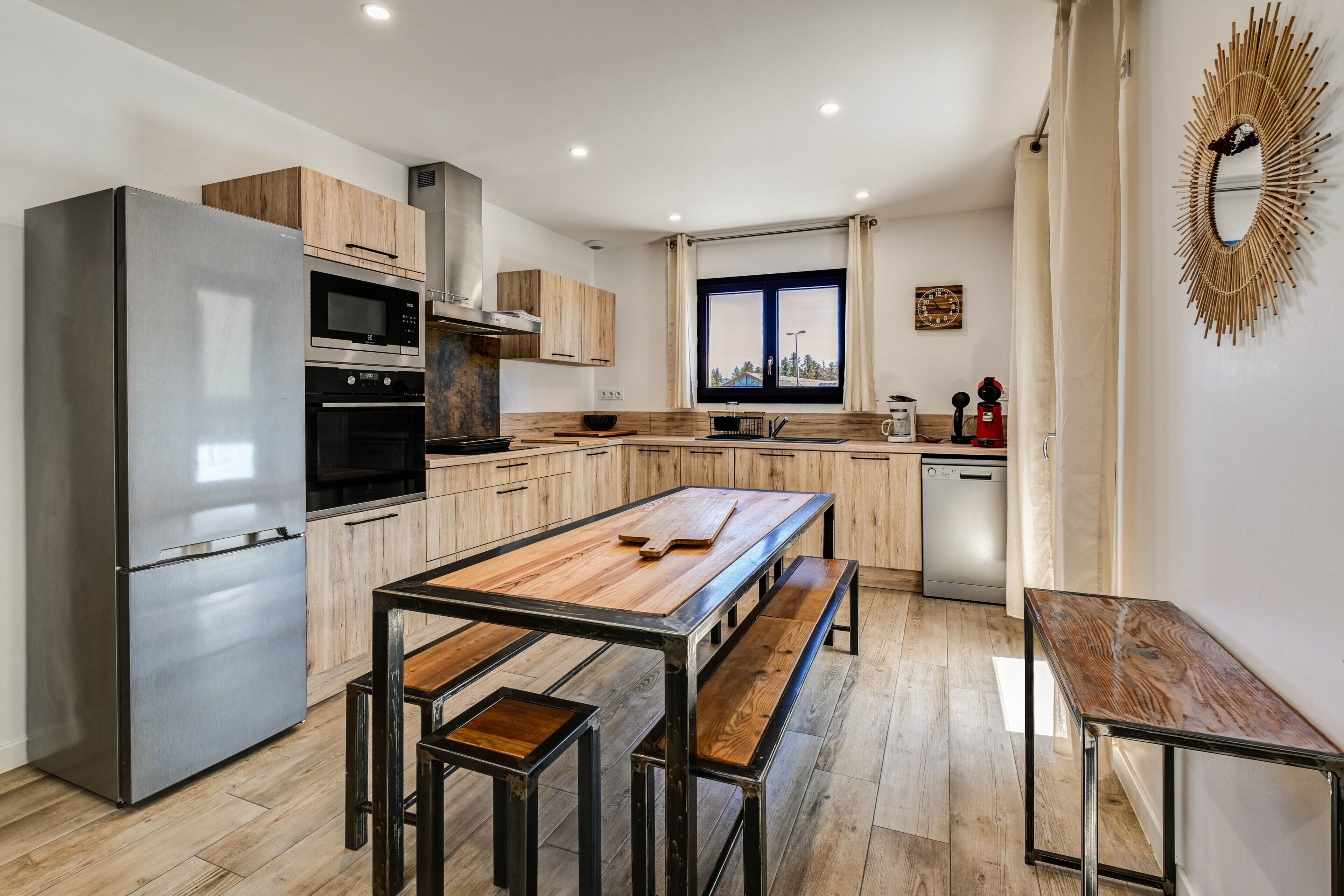 Une cuisine moderne dotée d’un réfrigérateur en acier inoxydable, de meubles en bois, d’un grand îlot central et d’un lave-vaisselle.