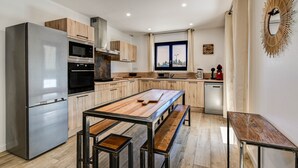 A modern kitchen with a stainless steel refrigerator, wooden cabinets, a large island, and a dishwasher.