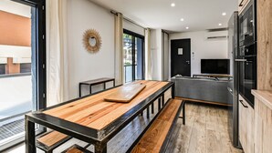 A modern kitchen with a wooden table and bench, a built-in oven, and a grey sofa.