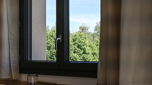 A window with a view of green trees, a door, and a small table with a glass.