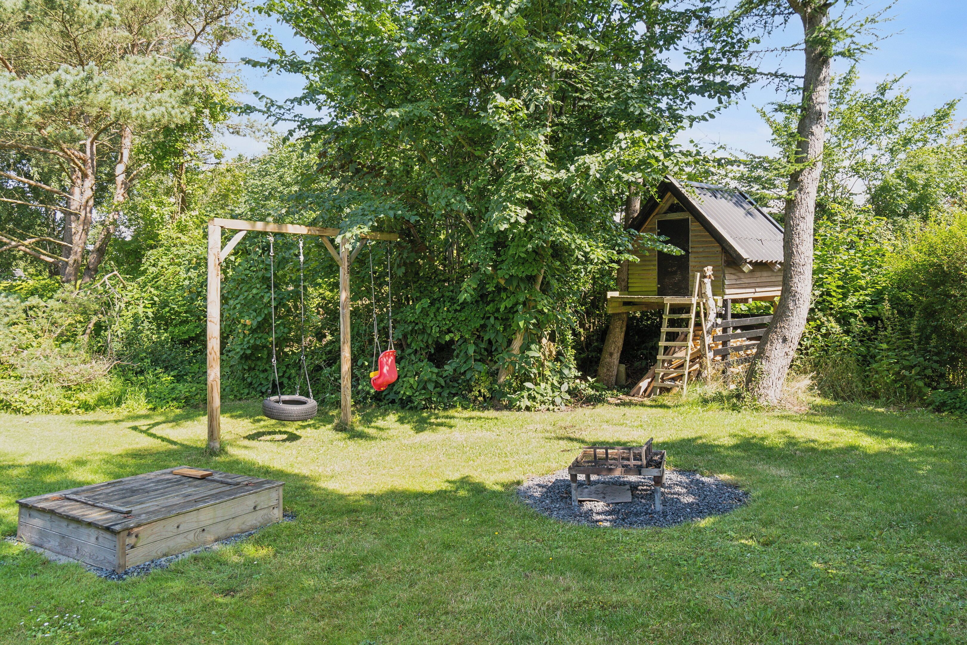 A rustic wooden cabin surrounded by lush greenery, a swing set, and a small fire pit.