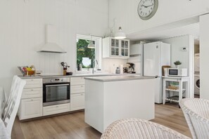 Una cocina moderna con armarios blancos, una isla central, electrodomésticos de acero inoxidable y un reloj en la pared.
