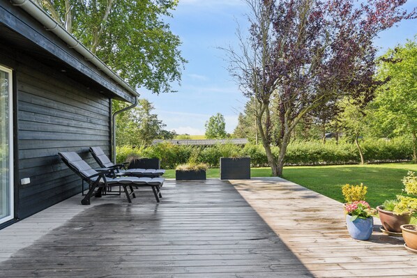 Una terraza de madera con sillones de descanso, una pérgola y plantas en macetas.