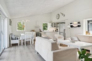 Un amplio espacio de estar con una mesa de comedor, mobiliario blanco y una cocina al fondo.