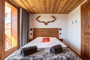 A bedroom with a wooden ceiling, a bed with a white bedspread, a red pillow, and two towels. - Apartment 'Appartement 10' with Mountain View and Balcony (Hauteluce)