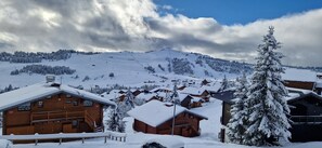Un pueblo cubierto de nieve con cabañas de madera, una pista de esquí al fondo y un abeto conspicuo.