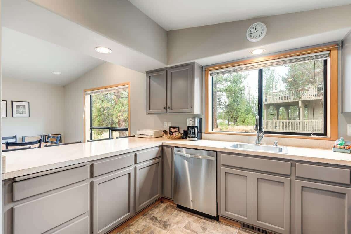 A modern kitchen with grey cabinets, a dishwasher, a coffee maker, and a window with a view of a deck.