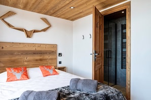 Une chambre à coucher avec une tête de lit en bois, deux oreillers orange, une couverture grise et une porte en bois.