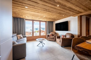 Un salon moderne avec un canapé, des fauteuils, une table basse et un téléviseur fixé au mur.
