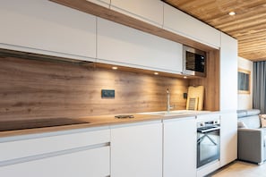 Une cuisine moderne avec des meubles blancs, un pare-feu en bois et des appareils électroménagers intégrés.