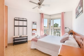 A bedroom with a bed, a bench, a ceiling fan, a window with curtains, and a balcony.