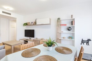 A modern living room with a dining table, chairs, a TV, and a bookshelf.